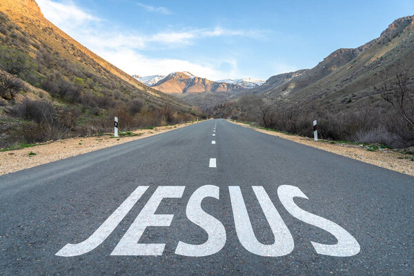 Asphalt road surrounded by mountains, Jesus written on the road. Christian concept. Jesus is the way