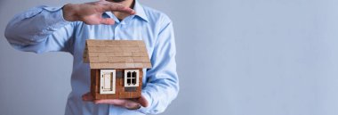 Gri sırt grubunda ev modeli tutan adam.