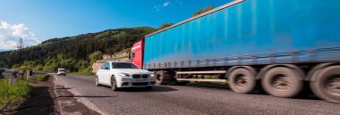 Kamyon ve araba mavi gökyüzünün altında yolda.