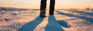 Adam güneşin altında karda yürüyor.