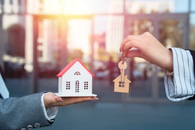 İki iş kadını, biri küçük ahşap bir ev tutuyor, diğeri anahtar, ev satışı, iş konsepti