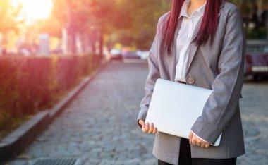 Female business office worker holding laptop, outdoors clipart