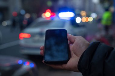 Arka planda polis arabası olan, elinde maket alanı olan bir telefon..