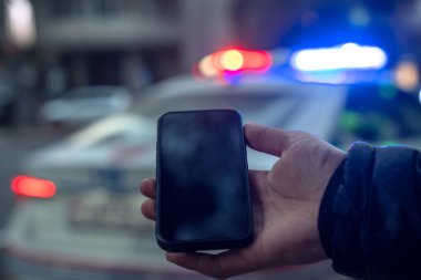 Arka planda polis arabası olan, elinde maket alanı olan bir telefon..