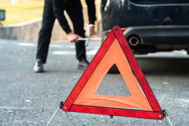 Bir adam araba lastiğini değiştiriyor, acil bir durum işareti..