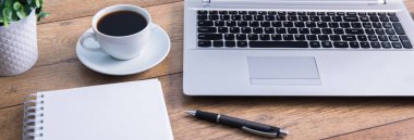 Not defterli bilgisayar ve çalışma masasında çiçekli kahve.