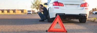 Acil dur levhası ve kırık arabanın yanındaki adam.