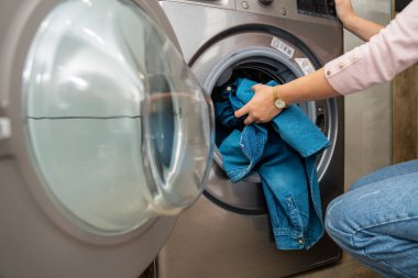 Ev hanımı çamaşır makinesi kullanıyor, çamaşırları makineye yüklüyor.