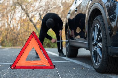 Bir adam araba lastiğini değiştiriyor, acil bir durum işareti..