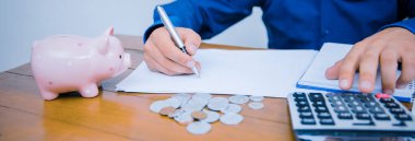Ofisteki hesap makinesiyle adamın elleri ve ahşap masadaki hesapları analiz eden finansal veriler..