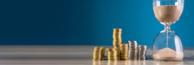 Bozuk paralar ve kum saatleri ahşap masada.