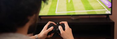 Bir adam evde monitörün önünde otururken joystick ile oynuyor.