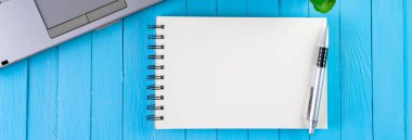 Diz üstü bilgisayar ve not defteri ahşap mavi masada.