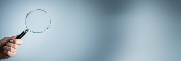 Holding a magnifying glass on a gray backgroun