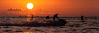 İnsanlar gün batımında denizde sörf yapıyor.
