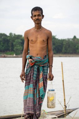 Riverside people of Bangladesh. A fisherman stands in the twilight horizon behind the river bank. clipart