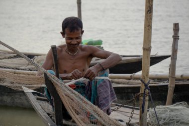 Gorai-Madhumati Nehri. Nehirde bir balıkçı teknesi. Bir balıkçı teknedeki balık ağını tamir ediyor. Sahne 24 Ekim 2023 tarihinde Rajbari, Bangladeş 'te çekildi..