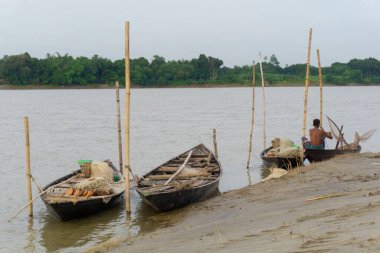 Gorai-Madhumati Nehri. Nehirde bir balıkçı teknesi. Bir balıkçı kayığın yanında kürek çekiyor.