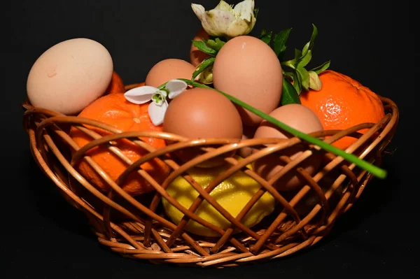 easter holiday, eggs, fruits   and flowers in  basket on black background