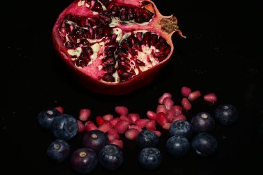 Siyah zemin üzerinde tohum ve yaban mersinli olgun kırmızı nar.