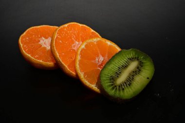 Siyah arka planda dilimlenmiş portakal ve kivi meyvesi.