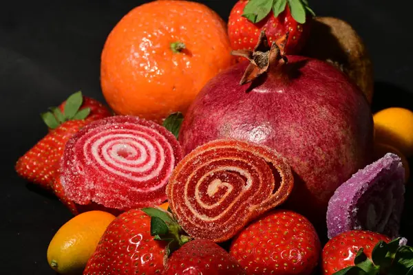 Siyah arka planda sarılmış jöleli bir grup meyve.