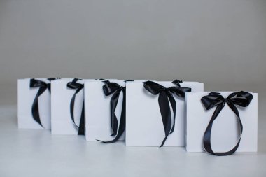 Five white paper gift bags with black bows on a gray background