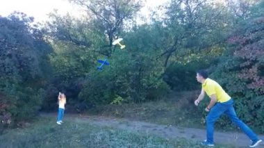 Father and child daughter launch yellow and blue foam planes gliders towards each other in a summer park