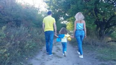 Aile - baba, anne ve kız Ukrayna bayrağıyla parkta el ele tutuşarak, mesafeye giderler.