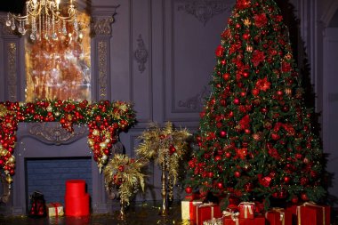 Kırmızı topları ve hediye kutularıyla kocaman bir Noel ağacı şöminenin arka planında, altın palmiyeler ve altın yıllanmış bir ayna