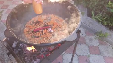 Özbek pilavı pişiriyorum. Izgarada dökme demir bir kazanda zirvak pişirmek. Ahşap el değirmeniyle biber ekliyorum.