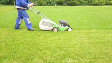 Bahçede çim biçme makinesiyle çimleri biçen özel takım elbiseli bir bahçıvan