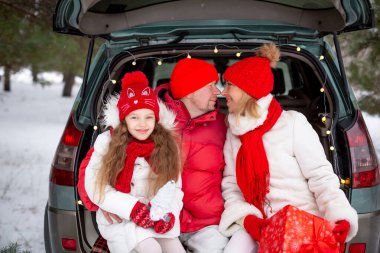 Aile - baba, anne ve kız mutlu bir şekilde ormanda Noel 'i kutluyor, bir arabanın bagajında oturuyor.