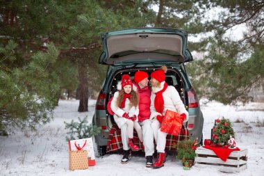 Aile - baba, anne ve kız mutlu bir şekilde ormanda Noel 'i kutluyor, bir arabanın bagajında oturuyor.