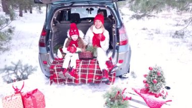 Aile - anne ve kız mutlu bir şekilde ormanda Noel 'i kutluyorlar, bir arabanın bagajında oturup sıcak çay içiyorlar.