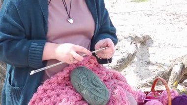 Bir kız nehir kıyısındaki bir ağacın köklerinde otururken yünden elbiseler örüyor.