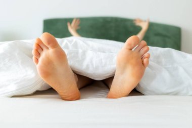 Female barefoot in close-up. Woman funny stretching lying on bed. White bedding. Dry soles. Concept of vacation and rest.