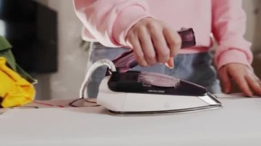 Close up of housewifes hands holds irons clothes on ironing board. Side view.