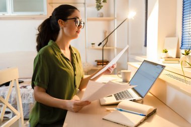 Side view of Caucasian young woman wearing glasses working at laptop. Student learning in home. Concept of remote work and freelancing.
