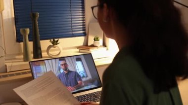 Videocall and online working. Back view of young Caucasian woman works at laptop. Remote work and freelancing.