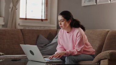 Freelance and remote work. Pretty young caucasian woman typing on laptop and sitting on sofa. Home office.