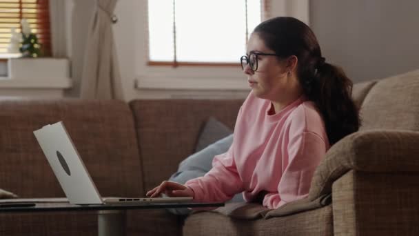 自由职业和远程工作 年轻漂亮的高加索女人 戴着眼镜躺在沙发上 用笔记本电脑 在总公司工作的家庭主妇 — 图库视频影像