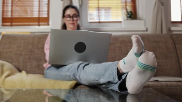 坐在沙发上舒舒服服地坐在笔记本电脑前工作的年轻白种人女人的袜子里 潘妮开枪了自由职业和远程工作的概念 — 图库视频影像