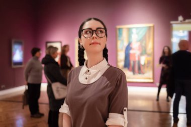 Portrait of young Caucasian pretty woman contemplates arts. Student visiting gallery or museum. Concept of education and culture.