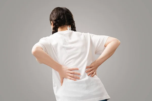 Back pain. The woman holds her hands to the small of her back. Rear view. Arthritis chondrosis. The concept of joint diseases.