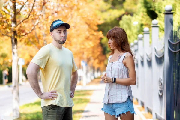 A young bearded guy and a girl with tattoos are quarreling on the street. Misunderstanding in a couple. The concept of relationship psychology.
