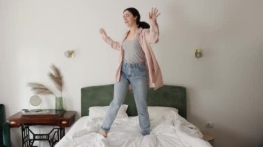 Happy young Caucasian woman funny dancing on bed. Slow motion. Concept of freedom and holiday