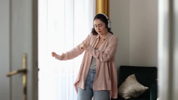 ヘッドフォンをしている若い白人の幸せな抑制されていない女性が踊っている ホームレジャー 楽しみと音楽演奏 — ストック動画