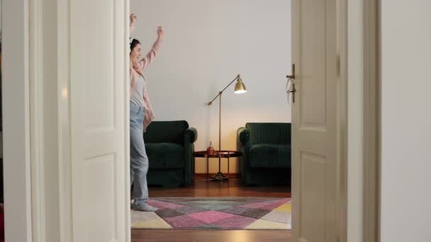 快乐的年轻白人女人戴着耳机走在房间里跳舞 从敞开的门看 家庭休闲 — 图库视频影像