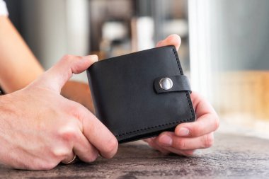 Male hands holds handmade black leather wallet. Advertising of craft leather accessories, close-up. Elegant fashionable holder.